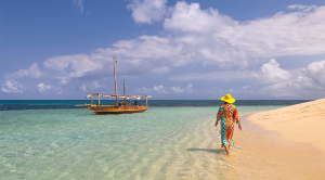 One tourist walking on the beach during a sunny day, with a boat in foreground, Zanzibar, Tanzania, Africa